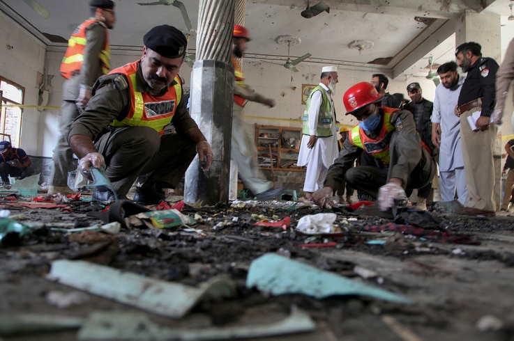 Pakistani rescue workers and police officers examine the site of a bomb explosion in an Islamic seminary, in Peshawar, Pakistan…