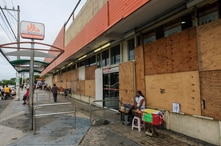 A woman waits for clients outside a supermarket with its windows covered with plywood as Tropical Storm Zeta approaches Cancun,…