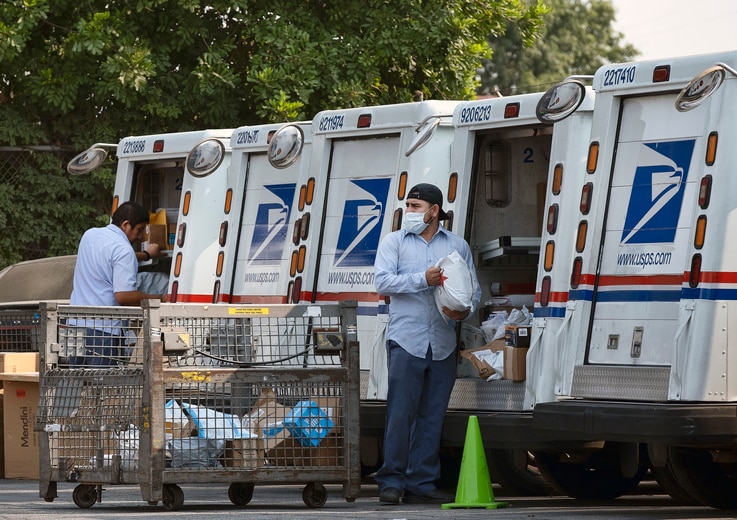 Postal workers load packages in their mail delivery vehicles at the Panorama city post office on Thursday, Aug. 20, 2020 in the…