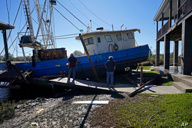 Boat owner Ricky Mitchell, left, surveys damage to his boat that Hurricane Zeta washed up against a home in Lakeshore, Miss., Oct. 29, 2020. 