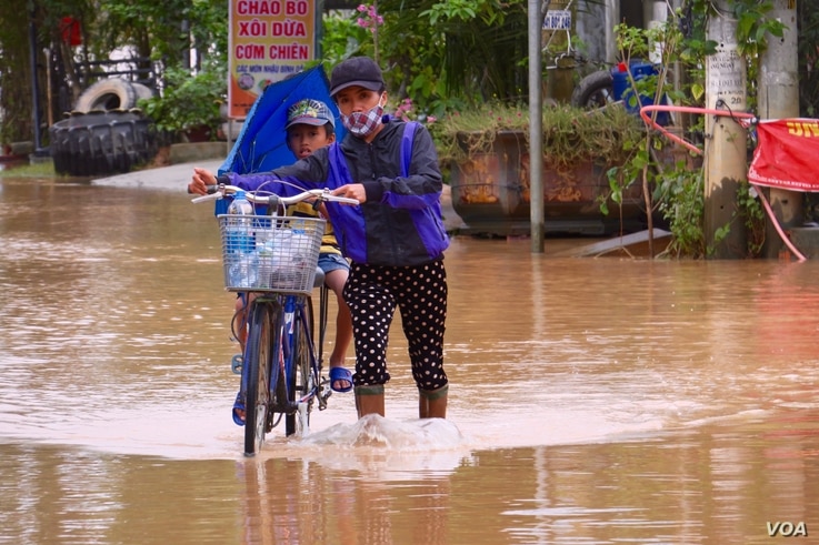 A woman pushes a child on a bicycle through a flooded street in Quang Tri.