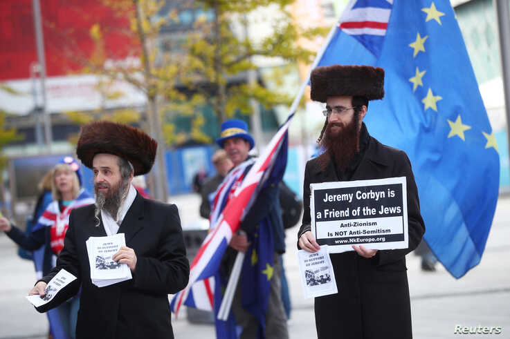 Two men wearing Orthodox Jewish attire hold placards and leaflets in support of Labour Party leader Jeremy Corbyn outside the…