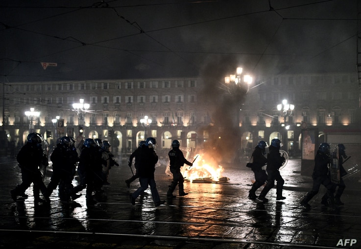 Police officers are seen in front of a garbage bin set on fire during a protest against new government restrictions to curb the spread of the coronavirus, in Turin, Italy, Oct. 26, 2020.