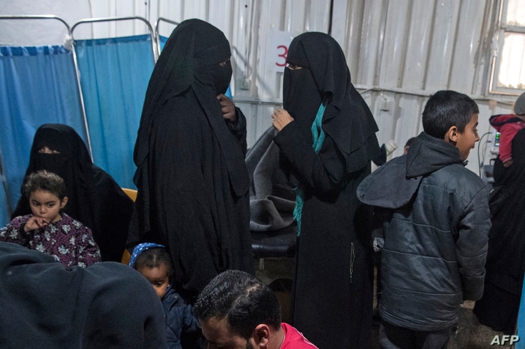 FILE - Two women, center, reportedly wives of Islamic State (IS) group fighters, wait with other women and children at a camp of al-Hol in al-Hasakeh governorate in northeastern Syria, Feb. 7, 2019.