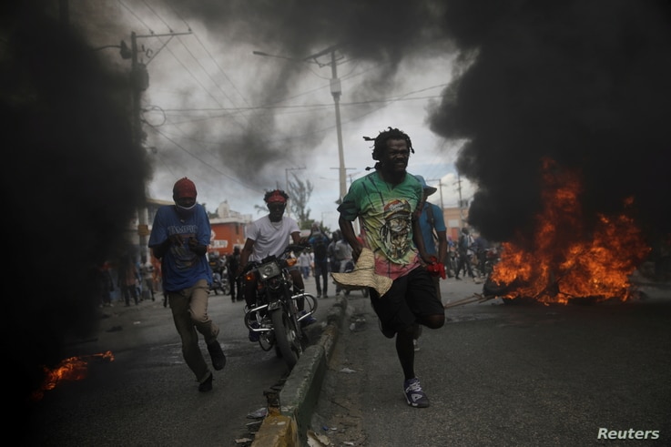 Protestors run past burning tires during a march demanding the resignation of Haiti's President Jovenel Moise.