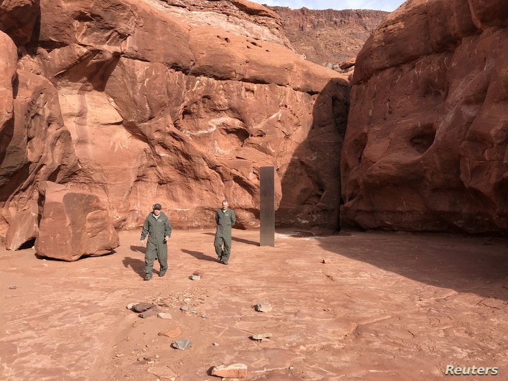 Utah Department of Public Safety Aero Bureau and Utah Division of Wildlife Resources crew members walk near a metal monolith…