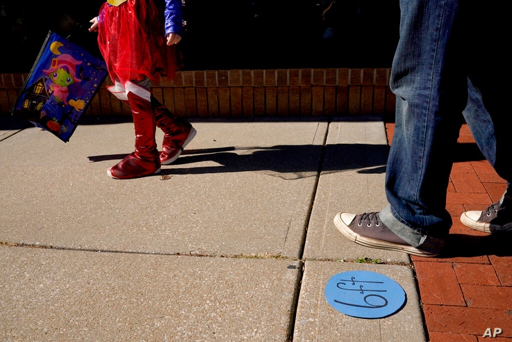 People walk past social distancing markers meant to help prevent the spread of the new coronavirus as they trick-or-treat for…