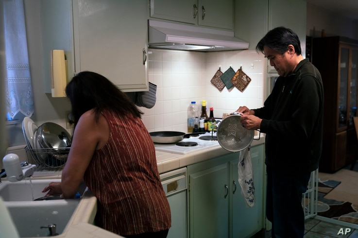 Kerry Osaki, right, helps his wife, Lena Adame, in the kitchen in Fountain Valley, Calif., Wednesday, Nov. 25, 2020. For years,…