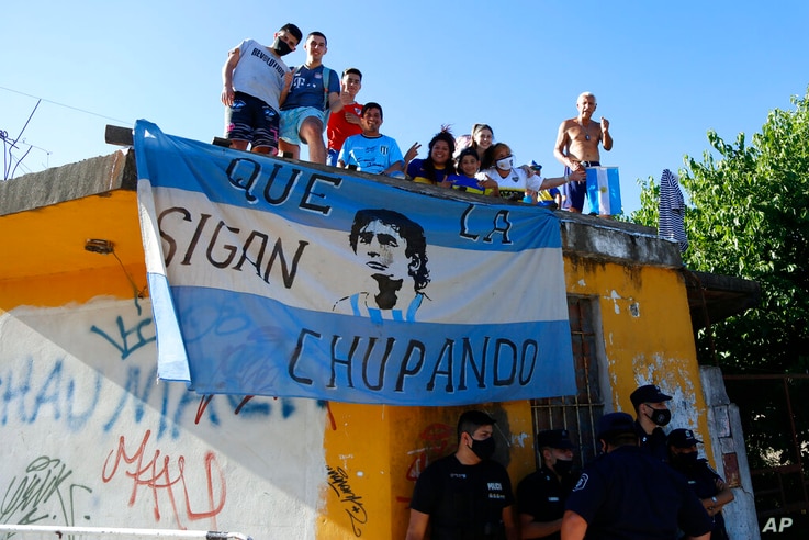 Fans stand on a roof of a house along the way of the motorcade carrying the remains of Diego Maradona to the Jardin de…