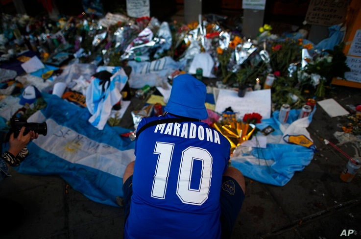 A fan mourns in front of flowers and posters left in tribute to Diego Maradona at the entrance of the Boca Juniors stadium…