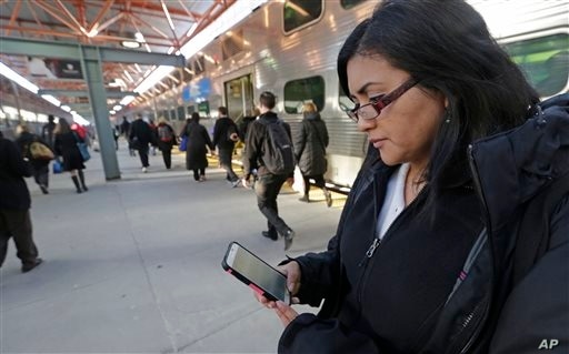 In this Friday, March 13, 2015 photo, Marilu Rodriguez checks a news website on her smartphone before boarding a train home at…