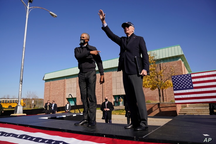 Democratic presidential candidate former Vice President Joe Biden, right, and former President Barack Obama greet supporters at a rally at Northwestern High School in Flint, Michigan, Oct. 31, 2020.
