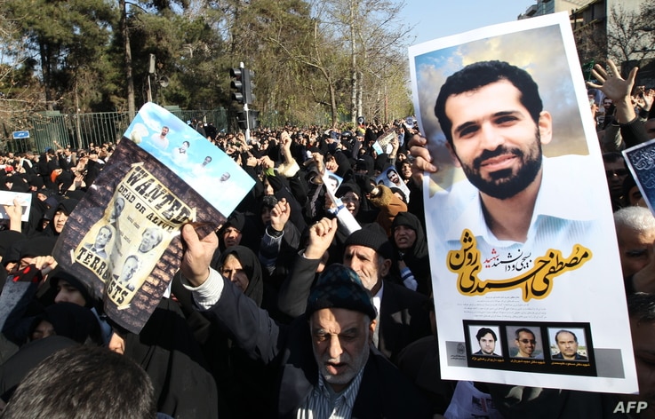 Iranians hold a portrait of assassinated nuclear scientist Mostafa Ahmadi-Roshan (R) and a wanted poster with portraits of US…