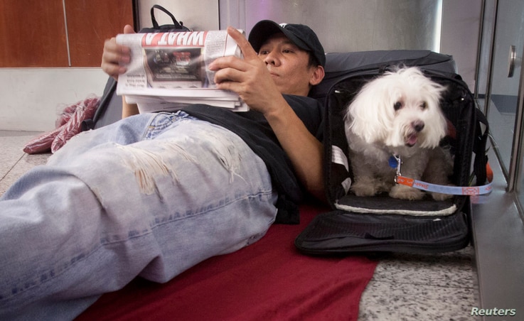 Stranded passenger Danny Nguyen and his dog Lucky wait as they spend the night on the floor of LaGuardia airport after his…