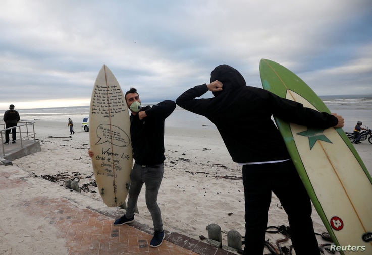 Surfers bump elbows as they protest against the nationwide lockdown regulations that allow exercise but not water activities,…