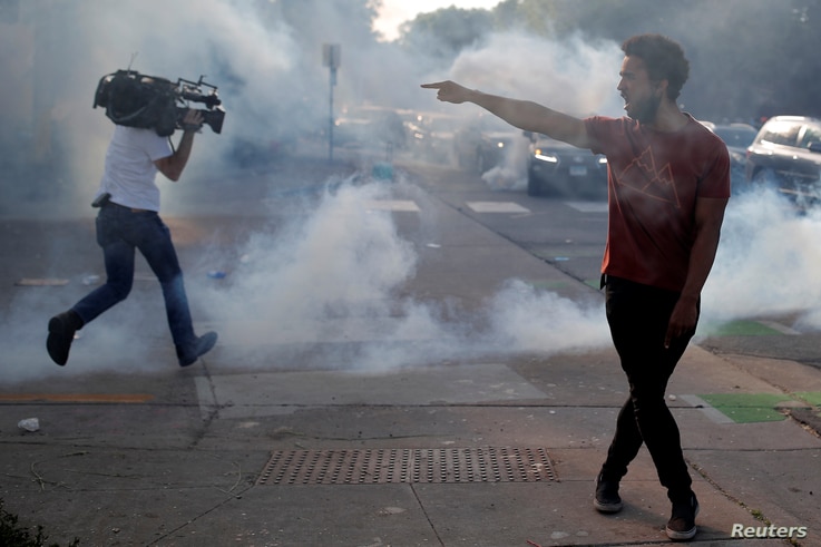 A protester argues with law enforcement officers as a reporter runs away from tear gas during a demonstration against the death…