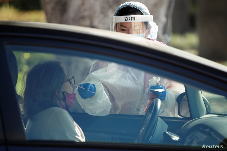 A healthcare worker at LAC USC Medical Center tests a person at a drive through testing center during the outbreak of the…