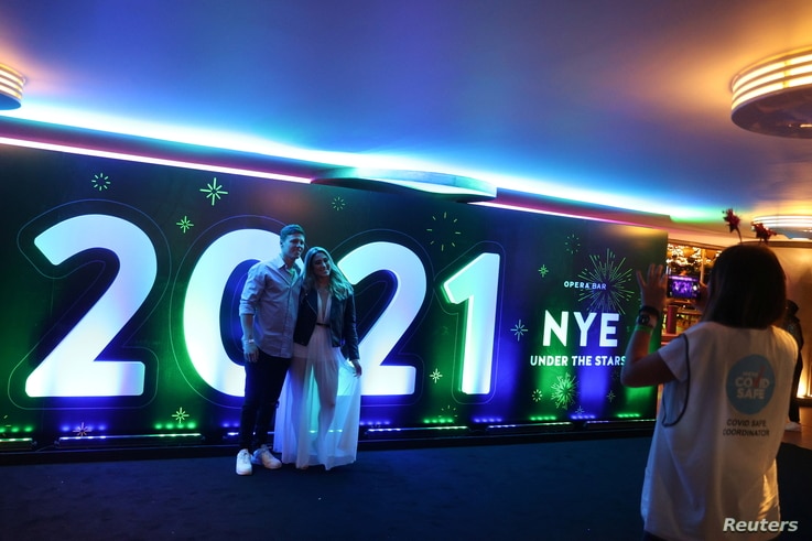 A man and woman pose for a photo in front of a 2021 sign as a limited number of people begin celebrating New Year's Eve at the…