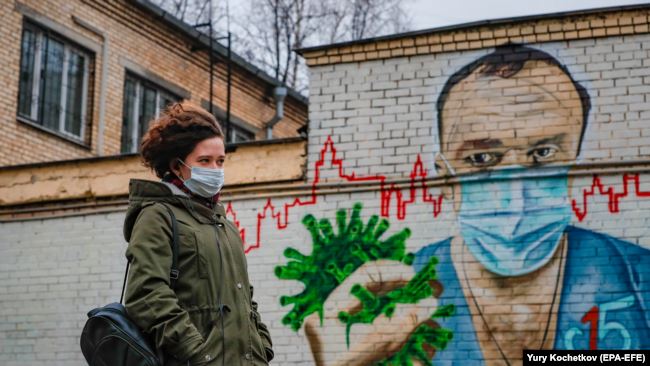 RUSSIA – A woman walks past a mural painting showing a doctor crushing the SARS-CoV-2 coronavirus in his hand, in Moscow, on November 19, 2020.