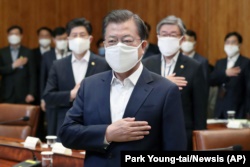 South Korean President Moon Jae-in wearing a mask salutes to a national flag at an emergency meeting on economic response to the coronavirus outbreak at the Presidential Blue House in Seoul, March 30, 2020