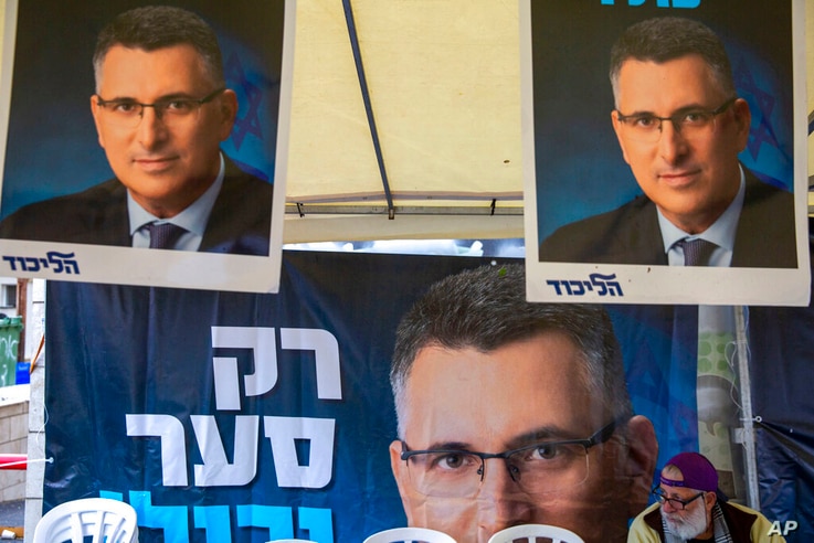 A Likud party member sits by a poster of veteran politician Gideon Saar from the governing Likud Party at a voting center in…