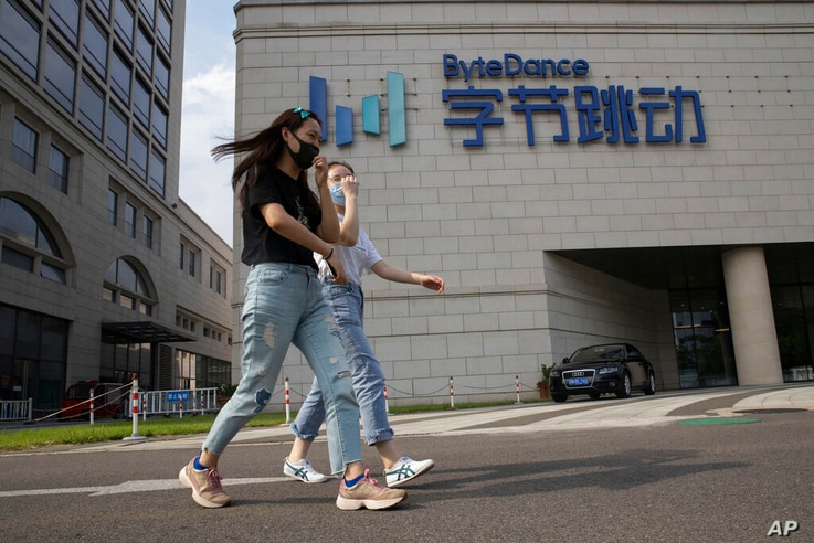 FILE - In this Aug. 7, 2020, file photo, women wearing masks to prevent the spread of the coronavirus chat as they pass by the headquarters of ByteDance, owners of TikTok, in Beijing, China.