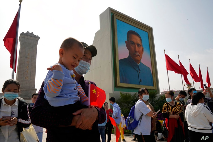 Tourists wearing masks to protect from the coronavirus stand near a portrait of Sun Yat-sen, who is widely regarded as the…