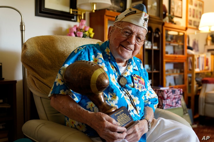 Mickey Ganitch, a 101-year-old survivor of the attack on Pearl Harbor, holds a football statue he was given.