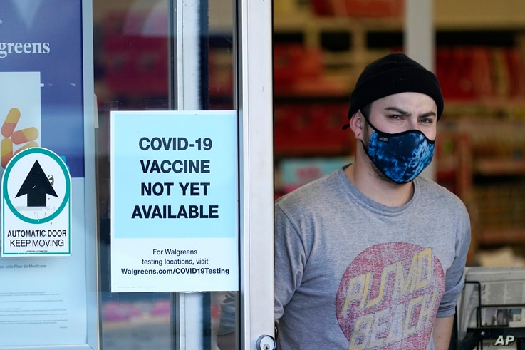 Customer wearing mask walks out of Walgreen's pharmacy store and past sign advising that COVID-19 vaccines are not available.
