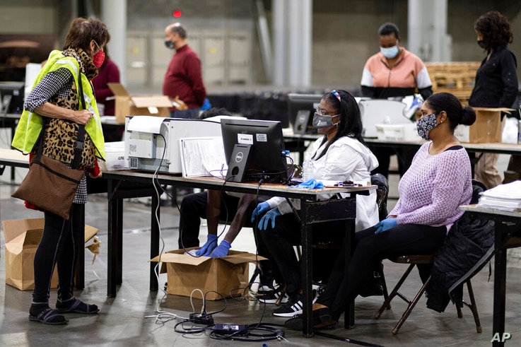 FILE - In this Nov. 25, 2020, file photo, a GOP observer, left, watches as workers scan ballots as the Fulton County…