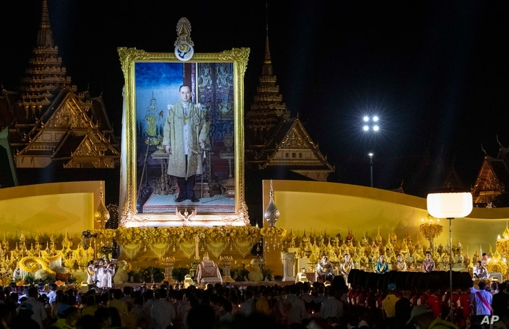 Thai King Maha Vajiralongkorn and members of the royal family sit in the aforeground of a giant portrait of late King Bhumibol…