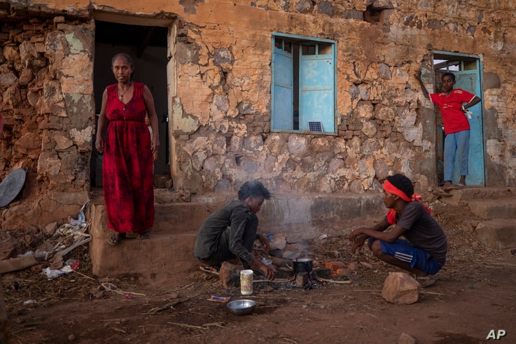 Tigrayans who fled the conflict in Ethiopia's Tigray region, start wood fires to prepare dinner, in front of their shelter.