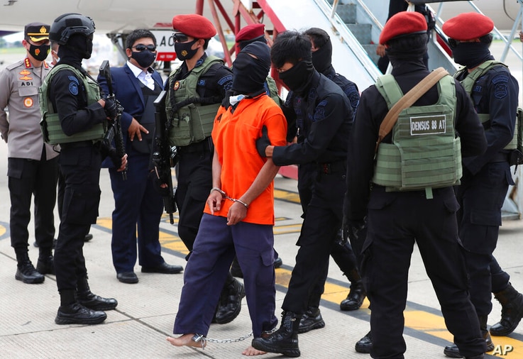 Police officers escort suspected militant Upik Lawanga, center, upon arrival at Soekarno-Hatta International Airport in…