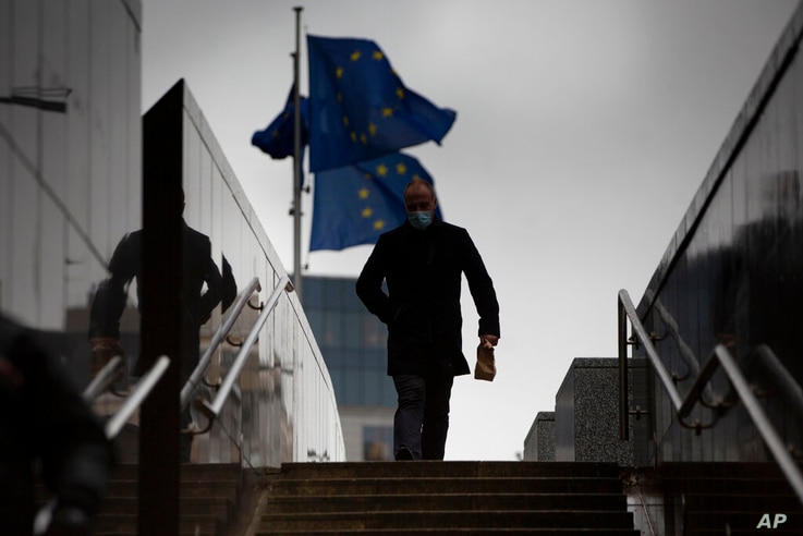 A man walks past EU flags flapping in the wind in front of the European Union headquarters in Brussels, Monday, Dec. 21, 2020…