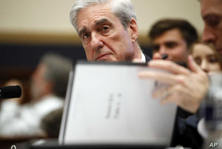 Former special counsel Robert Mueller, checks pages in the report as he testifies before the House Judiciary Committee