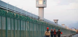 Workers walk by the perimeter fence of what is officially known as a vocational skills education centre in Dabancheng in…