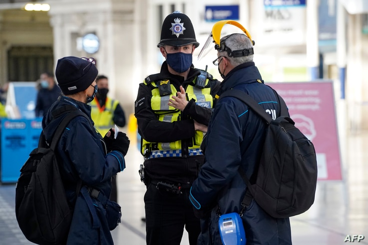 A member of the British Trasport Police speaks with travelers at Waterloo Station in London, Dec. 20, 2020.