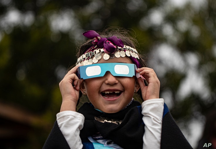 Magdalena Nahuelpan, a Mapuche Indigenous girl, looks at a total solar eclipse using special glasses in Carahue, La Araucania, Chile.