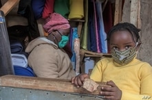 A woman who trades in fabrics, and her child, wears face masks as preventive measure against the COVID-19 coronavirus, in her…