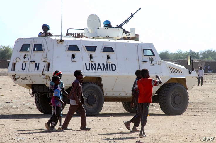 Sudanese children walk past an armoured vehicle of the United Nations and African Union peacekeeping mission (UNAMID) in Kalma…