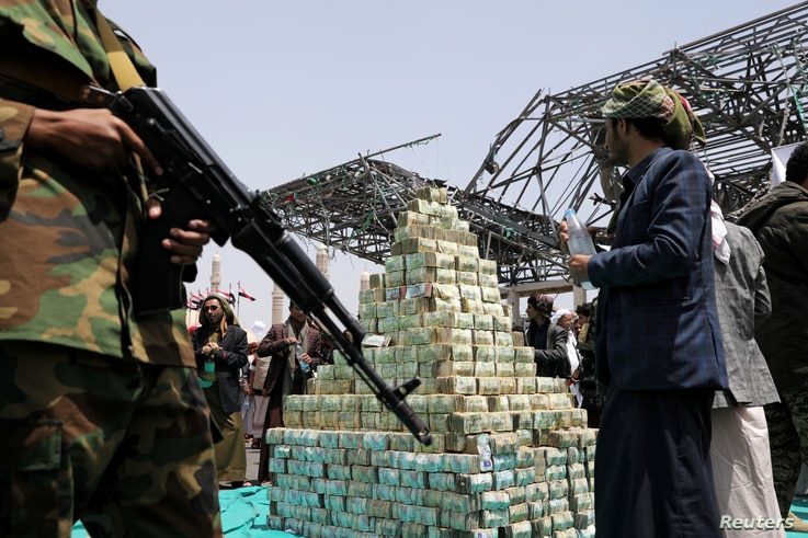 Houthi followers stand by bills of Yemeni currency during a ceremony held by Houthis to collect supplies for their fighters…