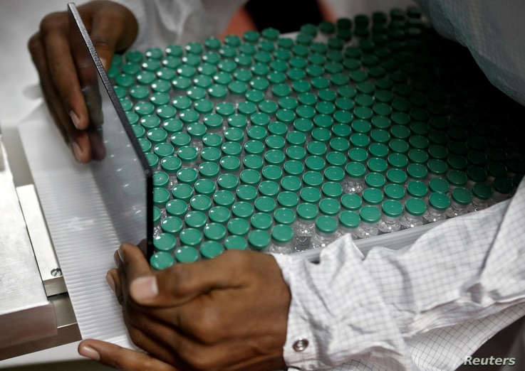 FILE PHOTO: An employee in personal protective equipment (PPE) removes vials of AstraZeneca's COVISHIELD, coronavirus disease …