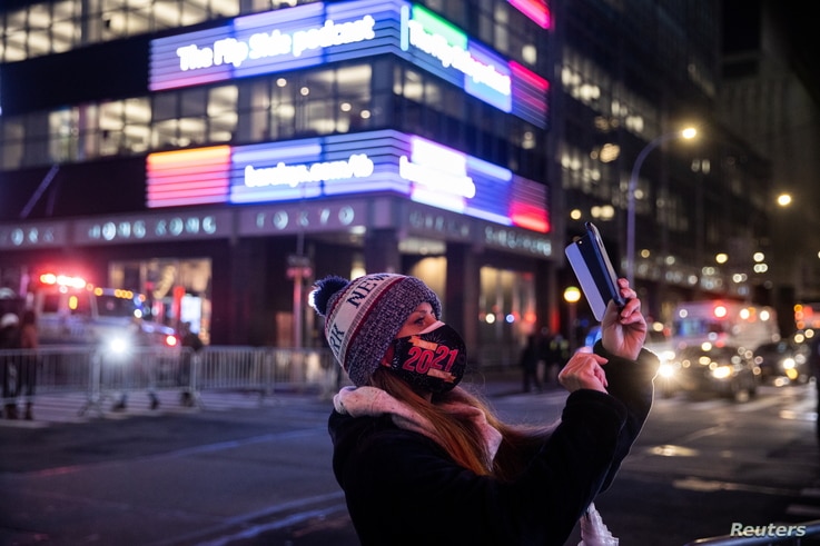 A woman wearing a protective mask takes a photo outside Times Square during the virtual New Year's Eve event following the…