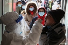 A medical worker in protective suit collects a swab from a resident during a mass nucleic acid testing following a recent…