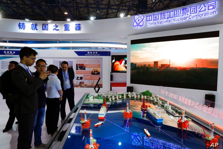 Staff members from the China National Nuclear Corporation attend foreign visitors as they look at the models of oil tanker…