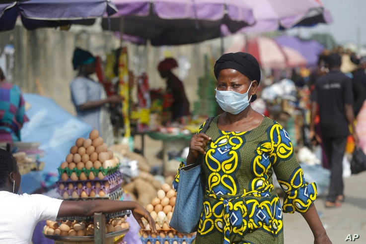 A woman wearing a face mask to protect against coronavirus, walks on a street, in Lagos, Nigeria , Thursday, Dec. 31, 2020. A…