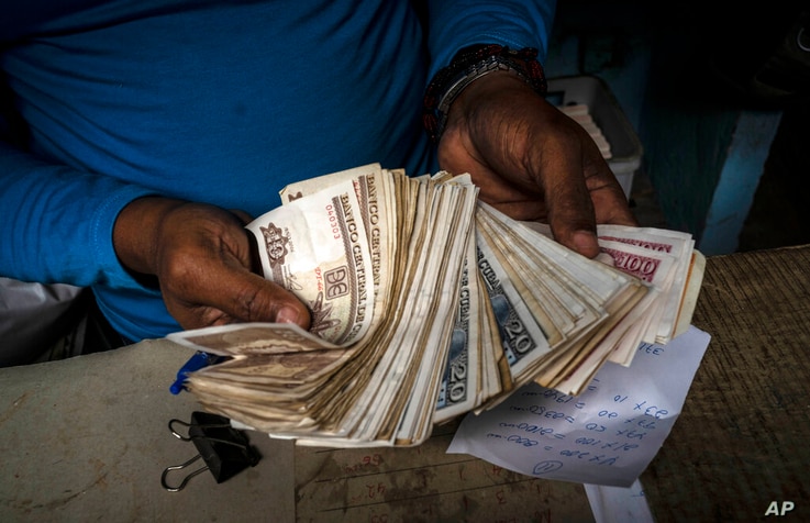 FILE - In this Dec. 11, 2020 file photo, a worker shows a wad of Cuban pesos in Havana, Cuba, Friday, Dec. 11, 2020. In 2021,…