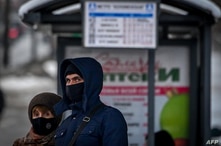 FILE - A man and a woman wearing face masks to protect against the coronavirus wait for a bus at a bus stop in central Moscow, Russia, Jan. 9, 2021.  