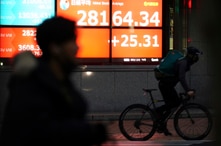 A man wearing a mask against the spread of the coronavirus rides a bicycle past an electronic stock board showing Japan's…
