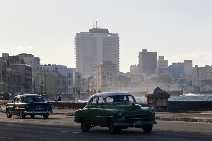 Vintage cars drive on the seafront boulevard El Malecon in Havana